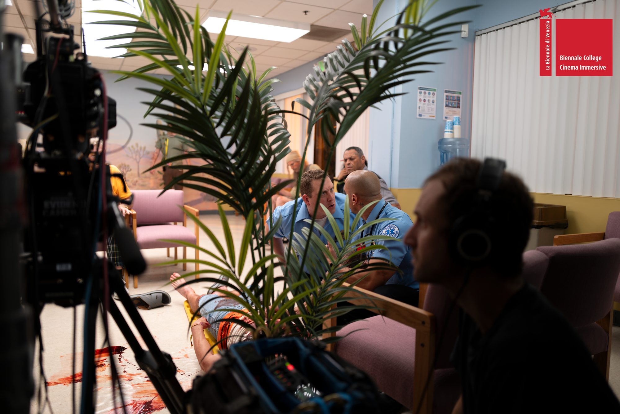A camera operator wearing headphones monitors a scene on the waiting-room set